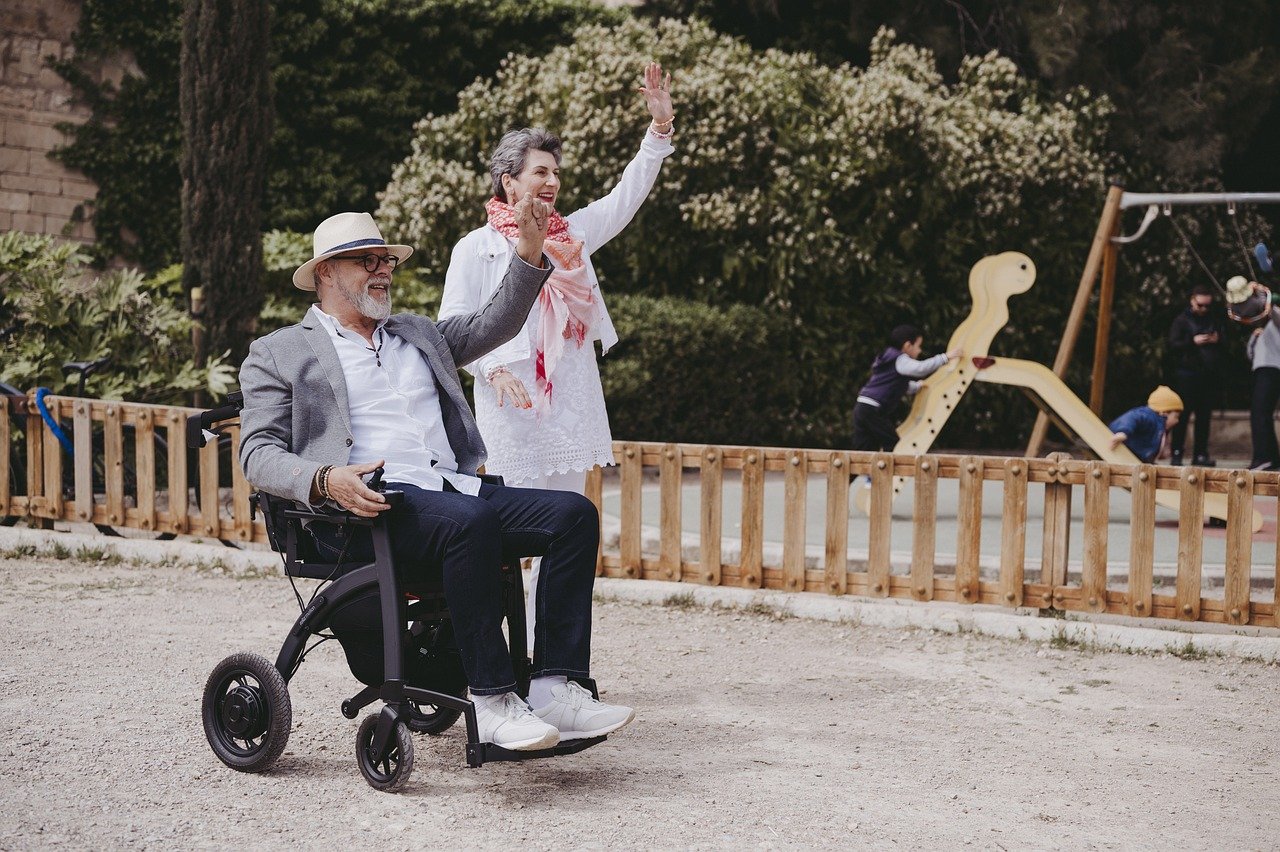 Man and woman waving, the man is in a small motorise wheelchair